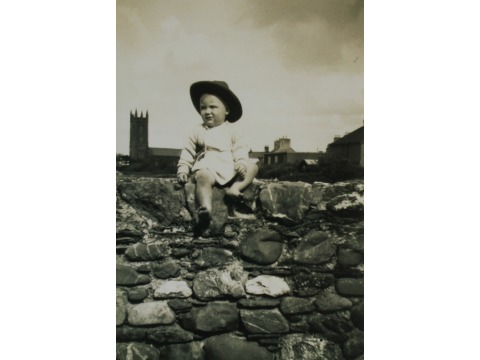 Mrs Joyce Kinley's eldest son Alastair sitting on a wall in Kirk Michael in 1954. Kirk Michael church is in the background