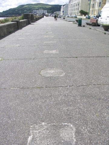 The patches in the walkway where the posts for the barbed wire once stood.
